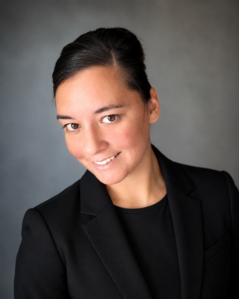 Professional woman in a black blazer smiling at the camera against a neutral gray background.